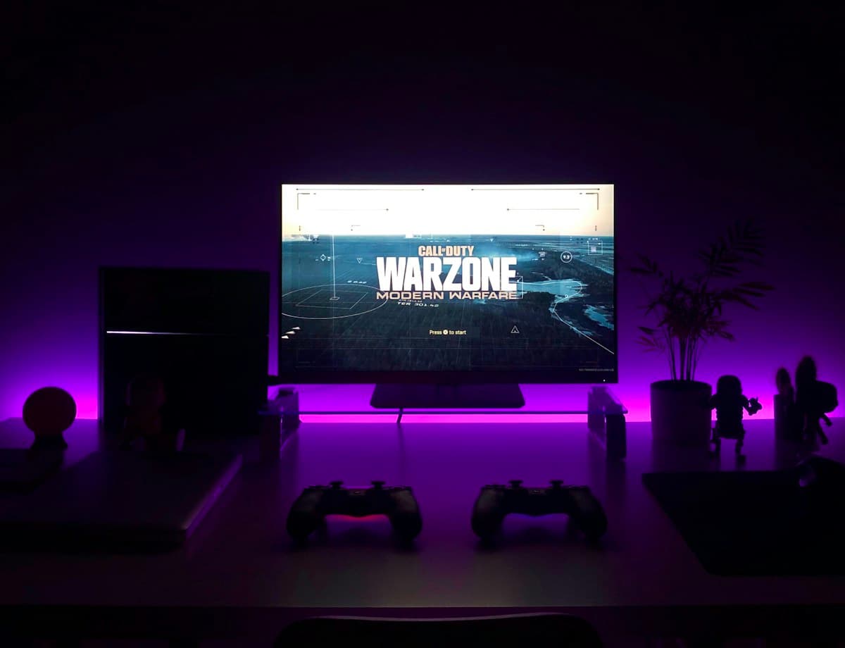 A gaming desk with a monitor, controllers, and purple ambient lighting